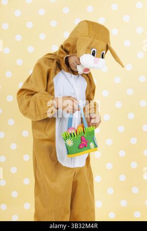 Kind verkleidet als Ostern Hase mit Korb Eiern auf gelben gestrichelten Hintergrund Stockfoto