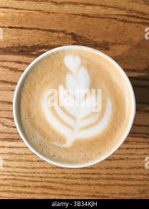 Blick von oben auf einen wunderschön gefertigten Latte mit eleganter Latte Art auf cremigem Schaum, serviert in einem gemütlichen Café. Perfekt für Themen der Kaffeekultur Stockfoto