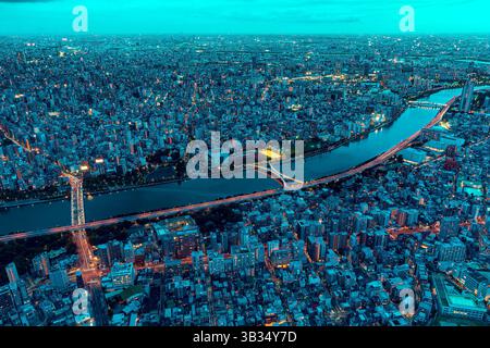 Aus der Vogelperspektive auf Tokio in der Abenddämmerung mit einer dichten, von Stadtlichtern beleuchteten Stadt. Ein breiter Fluss durchquert die Metropole Stockfoto