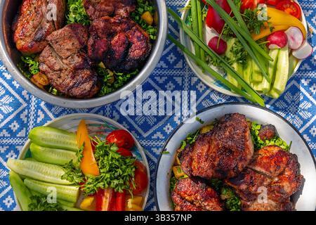 Nahaufnahme von gegrilltem Fleisch und frischem Gemüse auf dem Picknicktisch. Detaillierter Blick auf saftiges gegrilltes Fleisch und lebendiges frisches Gemüse. Stockfoto