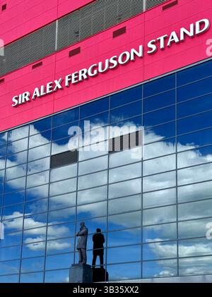 Sir Alex Ferguson steht im Old Trafford Football Stadium. Statue mit Wolken und blauem Himmel reflektiert in den Fenstern des Stands. Manchester, großbritannien Stockfoto