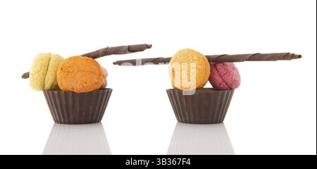 Frische Makronen in Schokoladentassen mit Stäbchen isoliert über weiß Stockfoto