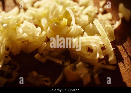 Nahaufnahme gehackter roher Zwiebeln auf einem hölzernen Schneidebrett. Detaillierte Aufnahme mit Textur und durchscheinenden Schichten frisch geschnittener Zwiebelstücke. Stockfoto