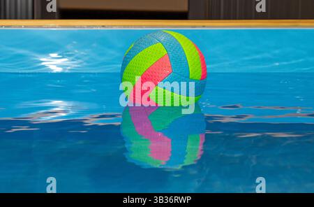 Farbenfrohe Plastikkugel, die auf einer Wasseroberfläche im Swimmingpool schwimmt Stockfoto