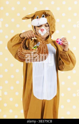 Kind verkleidet als Ostern Hase mit Korb Eiern auf gelben gestrichelten Hintergrund Stockfoto