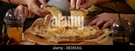 Gruppe von Freunden, die Käse-Pizza mit schmelzendem Käse und erfrischenden Getränken genießen und teilen, um einen Moment der Zweisamkeit und kulinarischen Köstlichkeiten festzuhalten Stockfoto