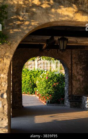 Steinbogen führt zum sonnigen Garten mit Blumen in Varenna, Comer See, Italien Stockfoto