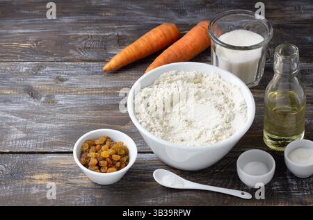 Set mit Zutaten für Karottenkuchen auf rustikalem Holztisch: Mehl, Zucker, Karotten, Rosinen, Öl. Hausbacken, Kochkonzept, natürliche Zutaten Stockfoto