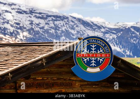 Dolomiten, Italien - 26.05.2024: Italienisches Skischulschild auf uriger Almhütte mit schneebedeckter Bergkulisse in St. Ulrich nahe dem Tal von Funes bei den Dolomiten Stockfoto