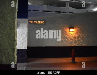 Weiße Wand in einer Tiefgarage mit beleuchtetem Kasino-Schild – urbanes Nachtleben und Kontrastkonzept. Stockfoto