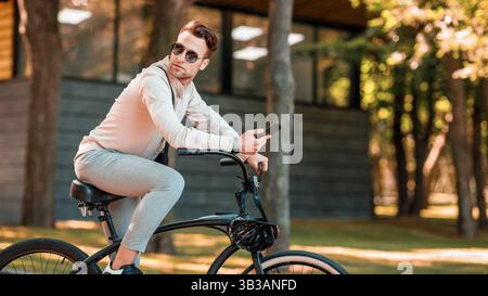 Geschäftsmann auf dem Fahrrad fahren. Kerl in Sonnenbrille und Smartphone im Park Stockfoto
