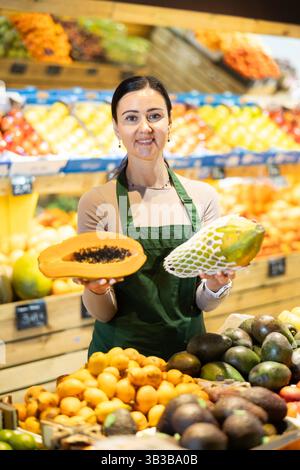 Weibliche Lebensmittelläden bieten Papaya in der Lebensmittelabteilung des Supermarktes an Stockfoto
