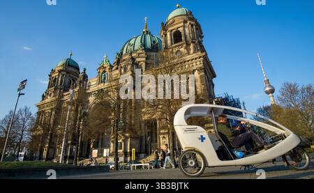 Rikscha-Fahrer wartet vor dem Berliner Dom, mit dem Fernsehturm im Hintergrund – moderner Tourismus in Berlin-Mitte. Stockfoto