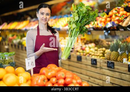 Weibliche Lebensmittelläden bieten Reifen Sellerie in der Lebensmittelabteilung des Supermarktes an Stockfoto