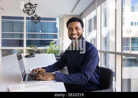 Porträt eines afrikanischen Mitarbeiters, der am Tisch sitzt und an einem Laptop arbeitet Stockfoto