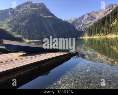 Ländliche Landschaft in den österreichischen Alpen in Tirol mit kristallklarem Alpensee umgeben von Natur und Bergen. Kleine Boote am Pier warten auf Touristen. Stockfoto