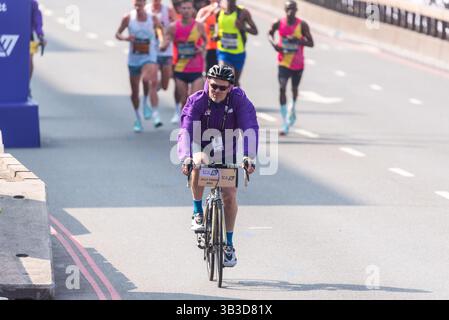 Ein zweiteiliger Motorradfahrer vor den Athleten, die 2025 beim TCS London Marathon teilnahmen, durch Tower Hill, London, Großbritannien. Offiziell Stockfoto