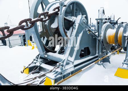 Das Anlegedeck eines Frachtschiffes mit Ankerwinden, einer Ankerkette an Winden, Pollern und Haws mit Anlegeseilen, gefroren und mit Schnee bedeckt. Sn Stockfoto
