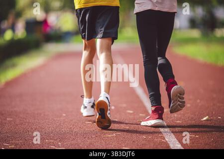 Vier Beine Nahaufnahme Bruder und Schwester in Turnschuhen laufen auf rotem Laufband in Laufstadionansicht. Zwei Läufer Kinder nebeneinander auf Th Stockfoto