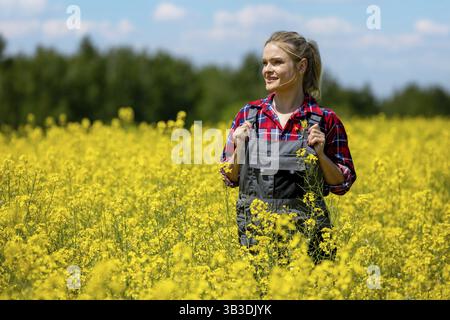 Eine fröhliche und fröhliche Frau steht glücklich inmitten eines riesigen Feldes leuchtender gelber Blumen unter einem hellen sonnigen Himmel Stockfoto