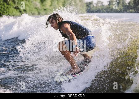 Aktive Wakesurfer springen auf Wake Board die Flußwellen hinunter. Surfer auf Welle. Männliches Training auf Wakesurf Training. Aktive Wassersportarten im Freien Stockfoto