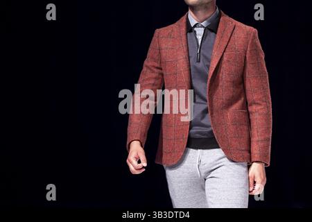Männliches Modell geht der Start- und Landebahn in roten Anzug während einer Modenschau. Fashion Catwalk Ereignis zeigt neue Sammlung von Kleidung. Single Modell isoliert auf einem Bla Stockfoto