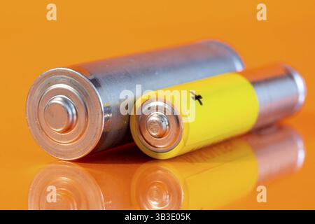 Eine gebrauchte AA- und eine AAA-Alkali-Mangan-Batterie sind auf einer reflektierenden orangefarbenen Oberfläche zu sehen. Nahaufnahme von der Plus-Seite der Batterien Stockfoto