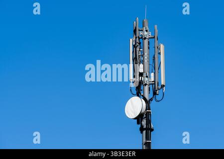 Ein hoher Kommunikationsturm steht vor einem hellblauen Himmel in einem städtischen Gebiet. Die Struktur ist mit verschiedenen Antennen ausgestattet, Facilitatin Stockfoto