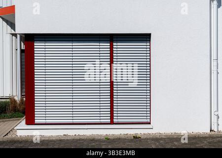 Geschlossene Alu-Jalousien schützen die Fenster eines modernen Gebäudes unter hellem Sonnenlicht. Die Struktur zeichnet sich durch klare Linien und eine minimalistische Ästhetik aus Stockfoto