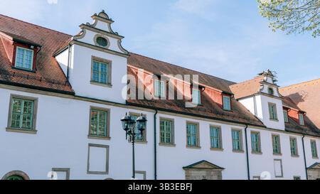 Historisches Gebäude mit einzigartigem architektonischem Design mit mehreren Fenstern, steilem, rot gefliestem Dach und dekorativen Giebeln unter klarem blauem Himmel. Bäume Stockfoto
