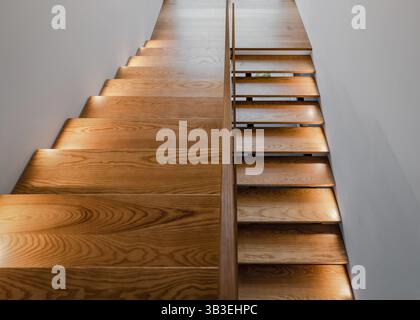 Holztreppe in einem Gebäude. Leere, nach unten gerichtete Treppe mit weißen Wänden. Foto in warmen Tönen. Stockfoto
