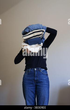 Frau, die einen ordentlichen Stapel gefalteter Pullover und Kleidung zu Hause hält. Stockfoto