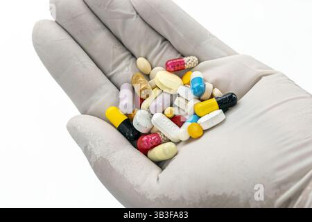 Pillen auf der Hand: Eine Nahaufnahme einer Hand mit Handschuhen, die eine vielfältige Auswahl an bunten Pillen zeigt. Eine Darstellung von Medizin, Gesundheitswesen und Behandlung. Stockfoto