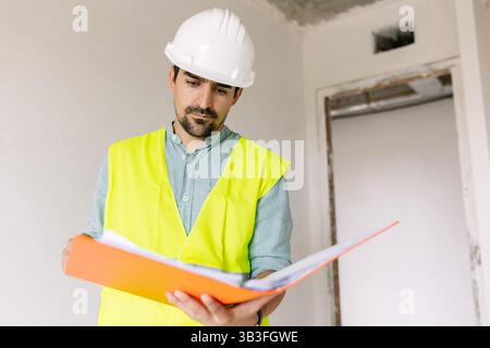 Der Vorgesetzte mit Schutzhelm und Sicherheitsweste überprüft die Dokumente auf der Baustelle Stockfoto