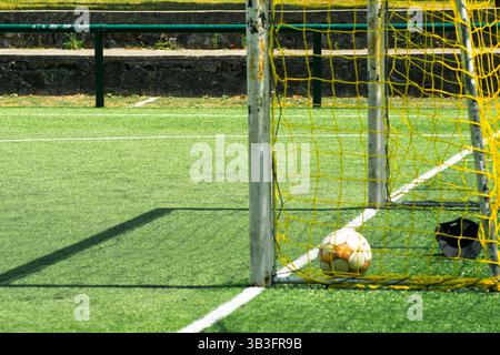 Ansicht eines Fußballballs auf einem synthetischen Feld in der Nähe des Tordetails eines Fußballballs in einem gelben Tor auf einem grünen Feld Stockfoto