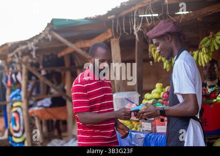 Person, die Früchte mit einer Kreditkarte bezahlt, während afrikanischer Obstverkäufer einen elektronischen POS-Automaten hält Stockfoto