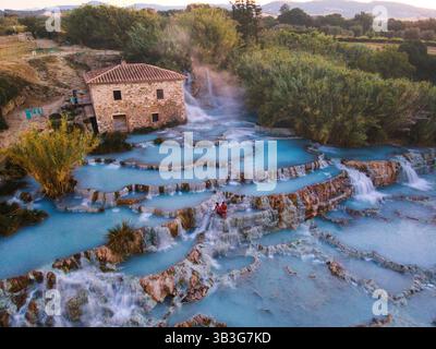 Türkisfarbenes Thermalwasser fließt nahtlos durch Terrassenfelsen und schafft eine malerische Landschaft in der Nähe eines alten Bauernhauses in Italien. Besucher entspannen sich in den warmen Quellen in Saturnia Toskana Italien Stockfoto