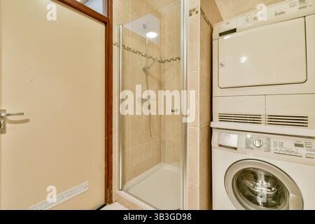 Ein kompaktes und modernes Badezimmer mit Glasdusche und gestapelten Waschmaschinen, das sauber und effizient gestaltet ist. Stockfoto