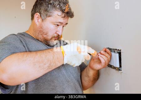 Elektriker arbeitet an der Befestigung des Wandschalters während der Renovierung des Zimmers in Wohnräumen. Stockfoto