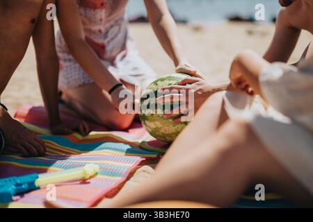Freunde teilen einen lustigen Moment mit einer Wassermelone an einem Strand am See Stockfoto