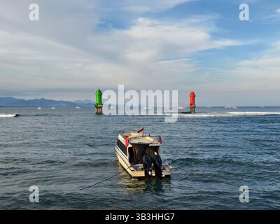Sanur, Bali, Indonesien – 23. April 2025: Ein Schnellboot liegt zwischen zwei Leuchtfeuern, einem grünen und einem roten, im Meer Stockfoto
