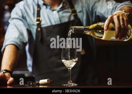 Sommeliermännchen gießt Weißwein in langstielige Weingläser. Stockfoto