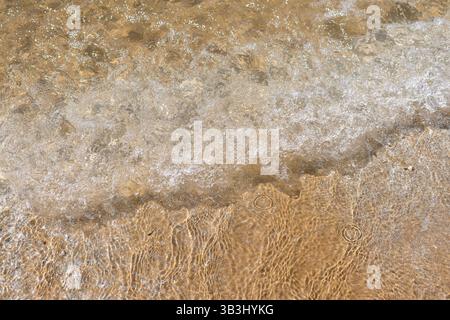 Eine Welle rollt auf einem Sandstrand Stockfoto