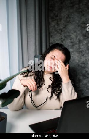 Müde kaukasische Frau, die sich aufgrund von Berufsproblemen gestresst fühlt. Irritations-Burnout. Scheuernde Augen. Umgang mit Arbeitsfristen. Ich habe nicht genug Schlaf. Stockfoto