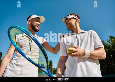 Zwei junge Männer teilen fröhliche Momente, während sie im Sommer gemeinsam Tennis spielen. Stockfoto