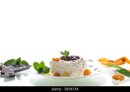 Hüttenkäse zum Frühstück auf einem Teller mit Schokoladensirup mit kandierten Früchten, isoliert auf weißem Hintergrund. Stockfoto