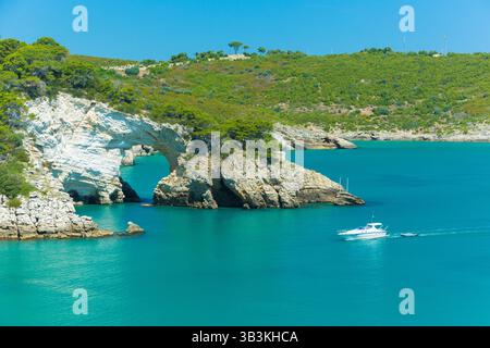 Touristenboot in der Bucht von San Felice mit einem Naturbogen (Architello) an der Küste von Gargano, Apulien, Italien. Stockfoto