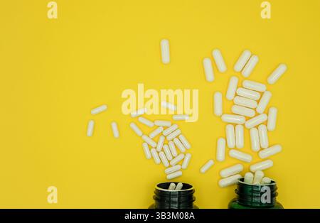 Nahrungsergänzungsmittel in Kapseln verschiedener Größen, die aus Flaschen auf eine gelbe Oberfläche gegossen werden. Draufsicht. Kopierbereich. Stockfoto