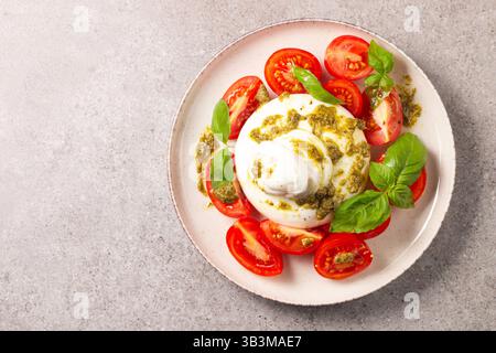 Burrata-Käse-Caprese-Salat mit Kirschtomaten, Olivenöl, Pesto und Gewürzen. Frischkost-Konzept. Stockfoto