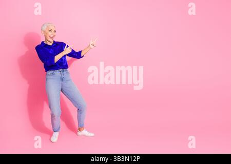 Stilvolle, reife Geschäftsfrau in trendiger Freizeitkleidung mit selbstbewusster Geste vor leuchtendem rosa Hintergrund Stockfoto